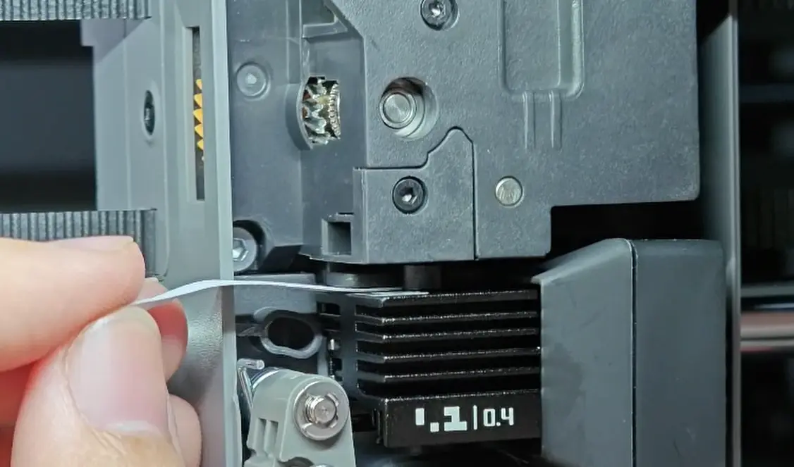 Foldet A4-papirstrimmel stikkes ind mellem dysespids og Nozzle Eddy Sensor for at kontrollere afstanden